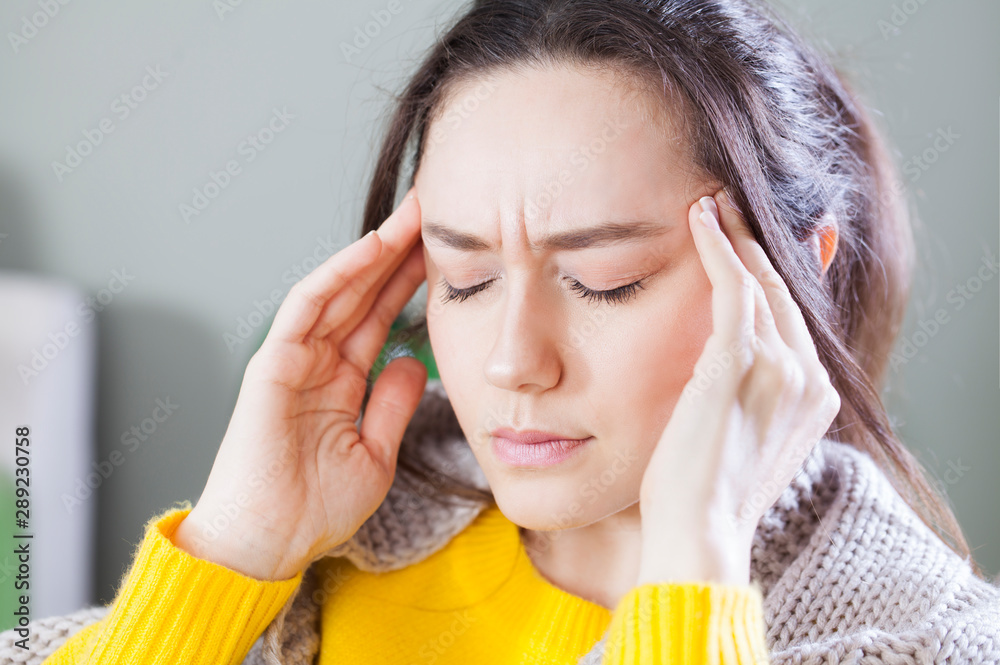 Wall mural Young woman with headache sitting on sofa