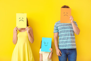 Family hiding faces behind emoticons against color background