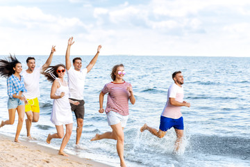 Happy friends running on sea beach at resort