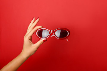 Female hand with stylish sunglasses on color background