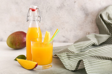 Glass and bottle of tasty mango juice on table