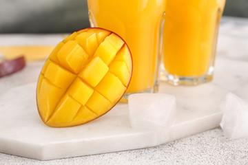 Tasty ripe mango and glasses of juice on table