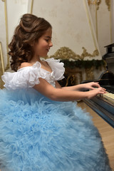 girl young princess in white with a blue dress and a barrette in black hair curls at the piano