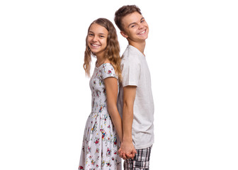 Portrait of smiling teen boy and girl standing back to back. Teenagers look at camera. Happy children hold hands together, isolated on white background. Friendship and love concept.