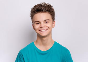 Portrait of happy teen boy in blue t-shirt in studio. Photo of adorable young smiling boy looking at camera on gray background. - 289239392