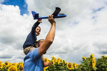 Father and son playing with a toy airplane near the sunflower field