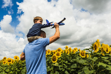 Father and son playing with a toy airplane near the sunflower field
