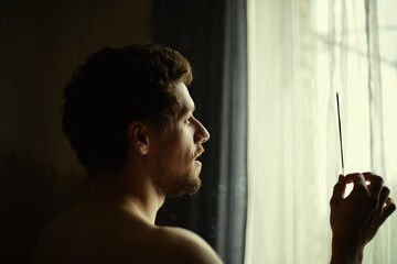 Handsome bearded male with muscles practicing yoga  indoors, using incense stick for calm and...