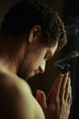 Handsome bearded male with muscles practicing yoga  indoors, using incense stick for calm and...