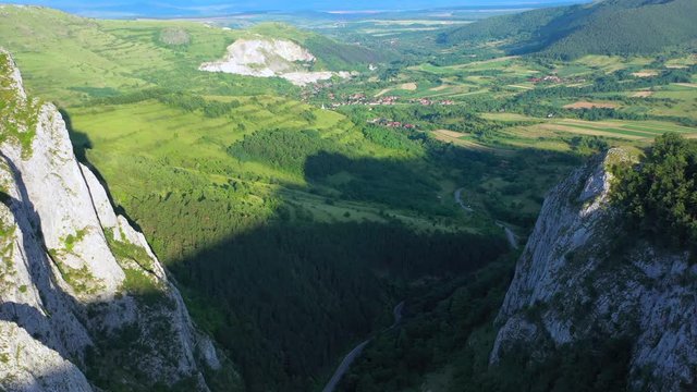 A wide angled fly over drone shot of the Coltesti mountain range, Romania. The valleys and gorges expand far into the distance, a windy road runs through the middle of the scenery.