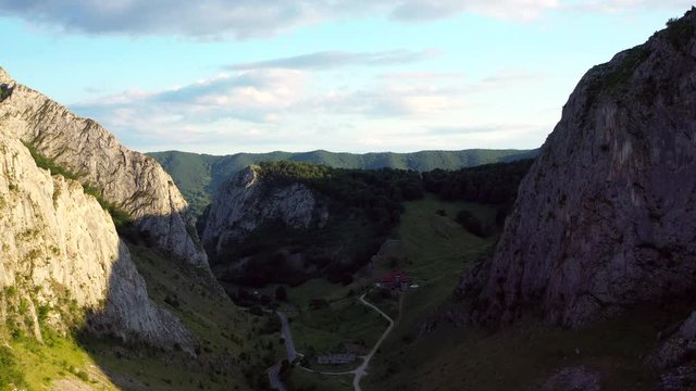 A wide angled fly over drone shot of the Coltesti mountain range, Romania. The valleys and gorges expand far into the distance, a windy road runs through the middle of the scenery.