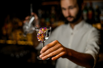Bartender with beard holds alcohol and strainer in glass