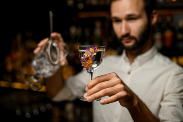 Bartender with beard holding alcohol and strainer in glass