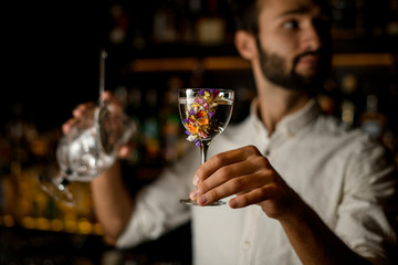 Bartender with beard holds an alcohol and strainer in glass
