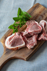 Raw lamb chops with freshly picked garden mint on a wooden chopping board.  Grey marl cloth background