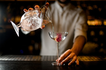 Bartender with beard holding a cocktail and strainer in glass