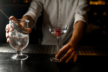Bartender holding cocktail and strainer on bar counter