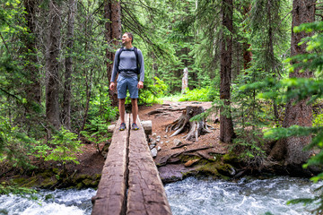 Mountain river stream with man crossing standing in rocky mountains in summer of 2019 on Conundrum Creek trail in Aspen, Colorado with wooden bridge - Powered by Adobe