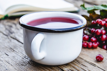 White mug or cup of hot viburnum tea on a wooden table near an open book and red viburnum berries. Source of natural vitamins. Used in folk medicine.