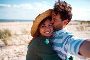 Happy traveling couple in love taking a selfie on phone at the beach on a sunny summer day.