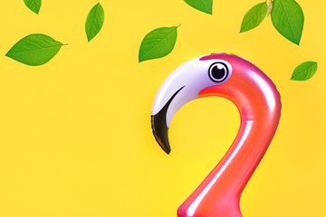 Summer fun concept with pink inflatable flamingo  head and falling green leaves on a yellow background with copy space
