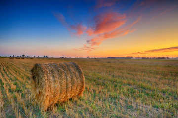 Beautiful summer sunset over fields with hay bales