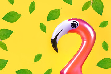 Summer fun concept with pink inflatable flamingo  head and falling green leaves on a yellow...