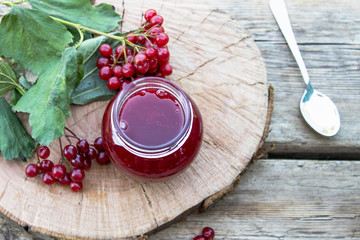 Viburnum fruit jam in a glass jar on a wooden table near the ripe red viburnum berries. Source of natural vitamins. Used in folk medicine.