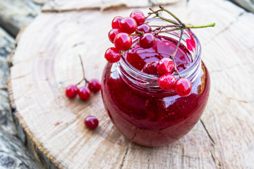 Viburnum fruit jam in a glass jar on a wooden table near the ripe red viburnum berries. Source of natural vitamins. Used in folk medicine.