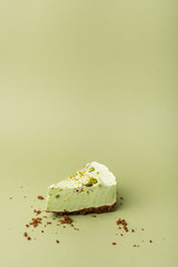 One slice of pistachio cheesecake on sight green background