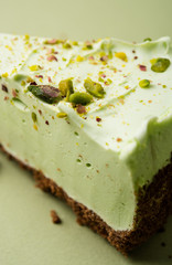 One slice of pistachio cheesecake on sight green background