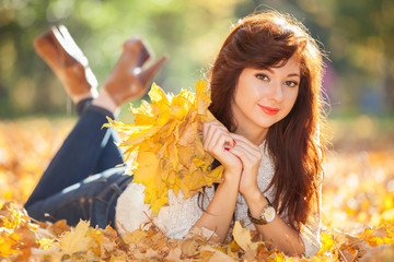 Young pretty woman relaxing in the autumn park. Beauty nature scene with colorful foliage background, yellow trees and leaves at fall season. Autumn outdoor lifestyle