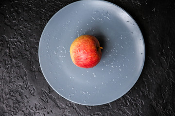 An apple lying on the grey plate. Still life photo. Black background.