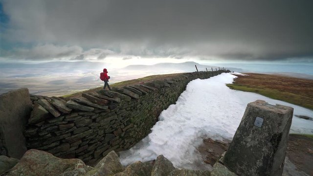 A hiker walking past the summit of Whernside, part of the Three Peaks in the Yorkshire Dales, England.