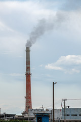 View of a complex of industrial buildings with smoking chimneys in the afternoon against the sky with clouds.