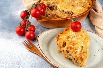 Golden cannelloni with meat, tomatoes, cheese sauce and pasta in alternating layers on a rustic plate