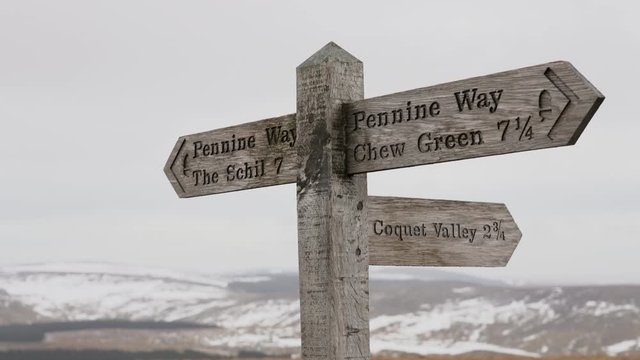 A close up of a wooden Pennine Way sign post in the wintery mountains and panning across the Cheviots at the border county of Northumberland