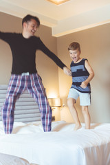 Happy father and son jumping on the bed.