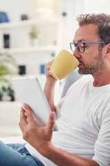 Man holding tablet, surfing online and drinking coffee.