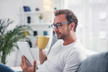 Man holding tablet, surfing online and drinking coffee.