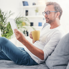Man holding tablet, surfing online and drinking coffee.