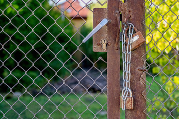 One lock and two padlocks on an old rusty gate.