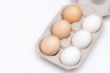 Three white and three brown eggs in a cardboard tray