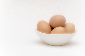 Whole brown eggs in a white bowl on a white surface
