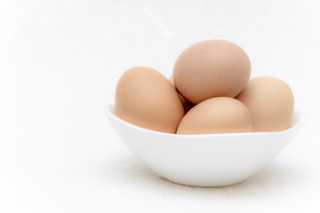 Whole brown eggs in a white bowl on a white surface