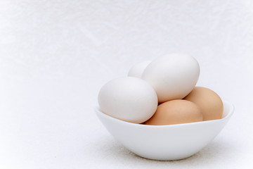Whole white and brown eggs in a white bowl on a white surface