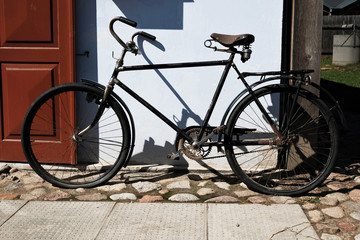 Fototapeta na wymiar vintage black bicycle parked outside old house with wooden door, casting strong shadows on white wall