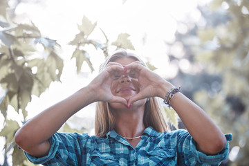 Young woman outdoors making heart - shape symbol for love and romance.
