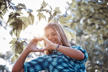 Young woman outdoors making heart - shape symbol for love and romance.