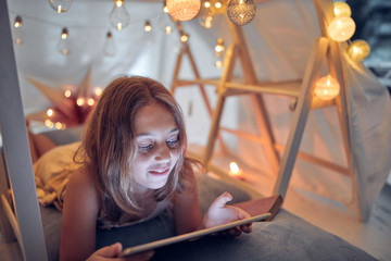 Little 10 year old girl using tablet under her home-made tent inside the living room.